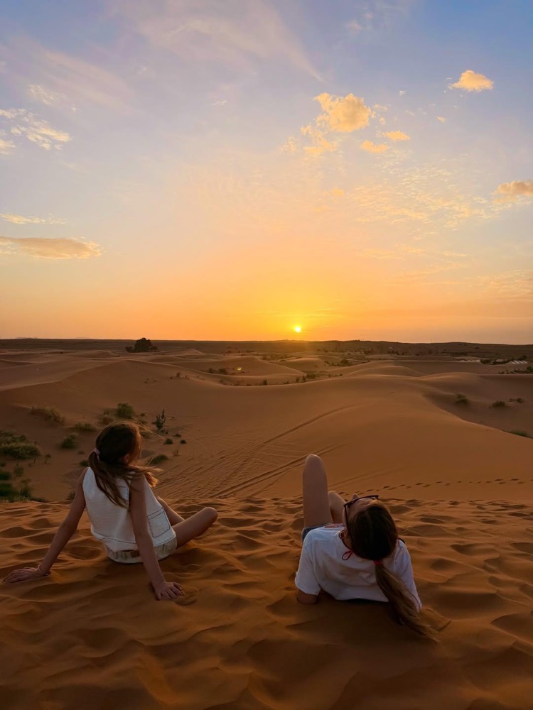 Dos viajeras viendo la puesta de sol sobre las dunas